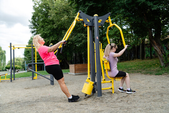 Women exercise at an outdoor gym in a park on a sunny day