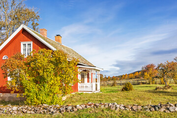 Idyllic red cottage in the countryside with a veranda with autumn colours in the garden © Lars Johansson
