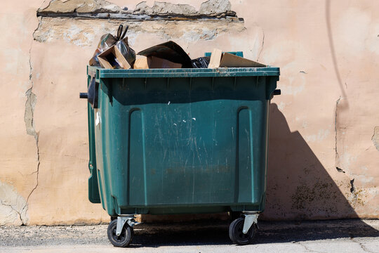 Green trash bin sits against cracked wall