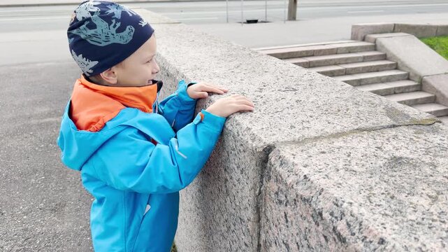 A young boy points excitedly over a granite wall in Saint Petersburg. He feels happy and curious during a peaceful day outdoors.