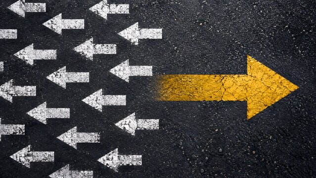 Yellow arrow pointing in the opposite direction of white arrows on asphalt representing leadership and breaking the mold