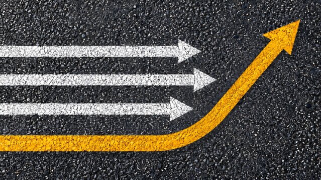 Yellow curved arrow diverging from straight white arrows on asphalt demonstrating a change of direction and alternative strategy