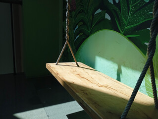 Empty wooden swing indoors by green mural in bright sun. © Suyono
