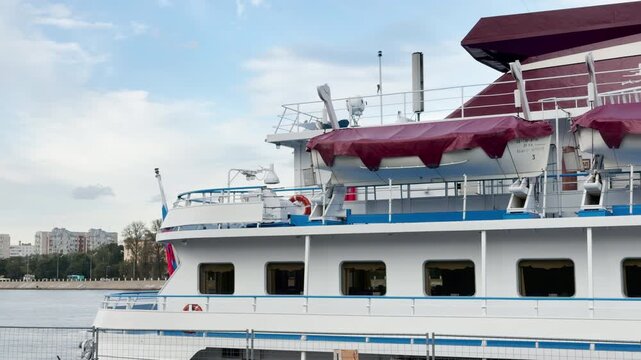A large cruise ship rests peacefully along the riverbank in Saint Petersburg. It waits quietly for an exciting trip under a cloudy blue sky. The view evokes a calm and hopeful feeling.