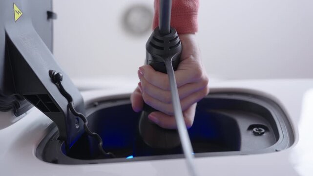 Hand of woman unplugs the charging cable of an electric vehicle (EV car), Sustainable clean energy