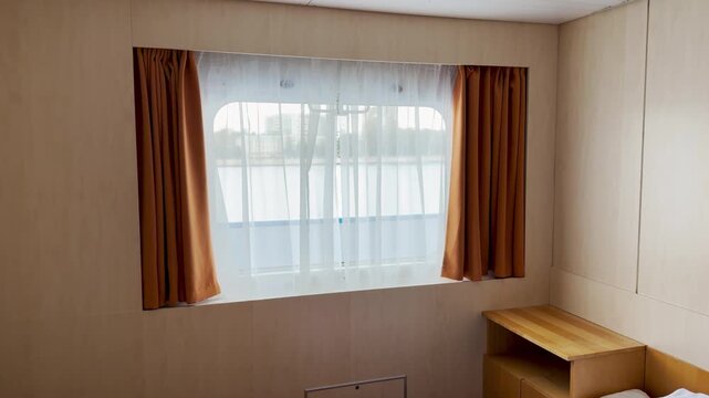 A cozy window with curtains looks out from a cruise ship cabin on the Neva River. Soft daylight shines through sheer fabric. The peaceful room fills with a warm and serene feeling.