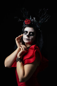 Day of the Dead or Halloween themed image with a woman with skull painting on her face and a skull.	