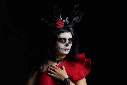 Day of the Dead or Halloween themed image with a woman with skull painting on her face and a skull.	