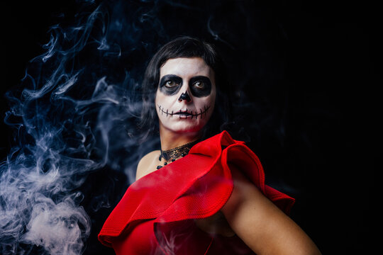 Day of the Dead or Halloween themed image with a woman with skull painting on her face and a skull.	