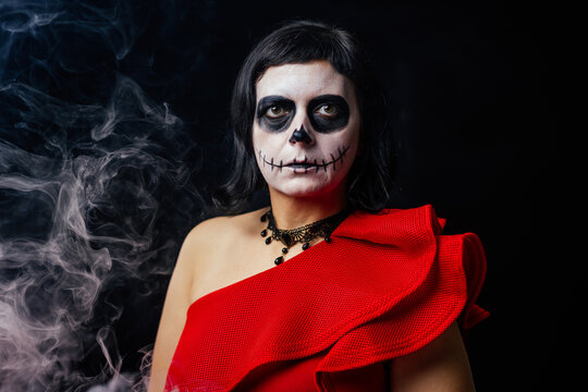 Day of the Dead or Halloween themed image with a woman with skull painting on her face and a skull.	