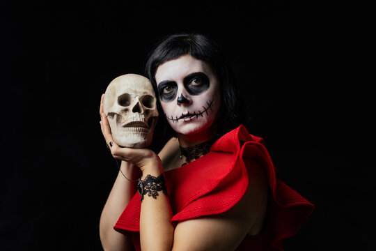 Day of the Dead or Halloween themed image with a woman with skull painting on her face and a skull.	