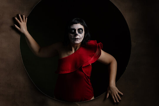 Day of the Dead or Halloween themed image with a woman with skull painting on her face and a skull.	