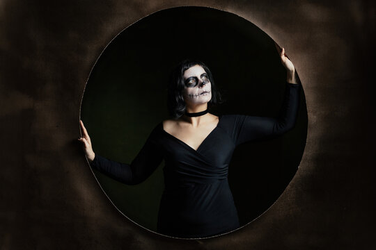 Day of the Dead or Halloween themed image with a woman with skull painting on her face and a skull.	