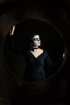 Day of the Dead or Halloween themed image with a woman with skull painting on her face and a skull.	