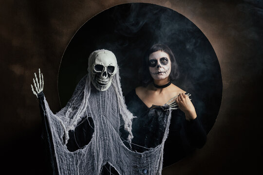 Day of the Dead or Halloween themed image with a woman with skull painting on her face and a skull.	