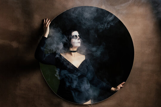 Day of the Dead or Halloween themed image with a woman with skull painting on her face and a skull.	