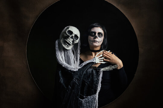 Day of the Dead or Halloween themed image with a woman with skull painting on her face and a skull.	