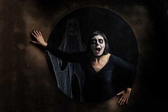 Day of the Dead or Halloween themed image with a woman with skull painting on her face and a skull.	