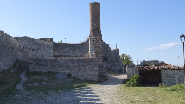 Stone walls and the Red Mosque minaret rise above a cobbled path inside Berat Castle under clear daylight.