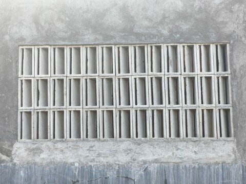 Rectangular concrete breeze block vent lattice mounted on a raw unfinished cement wall providing airflow ventilation in a house building
