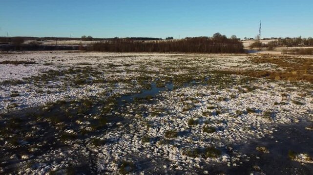 Snow-covered grassland and reeds in winter wetland near Ega Engso lake wetland, Aarhus, Denmark, aerial dolly natural serene backdrop, people walk on path in backdrop
