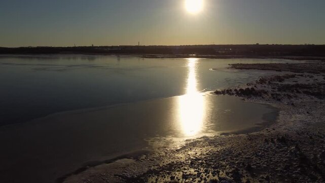 Low winter sun reflects across frozen Ega Engso lake wetland near Aarhus, Denmark, aerial orbit of glowing ray beam