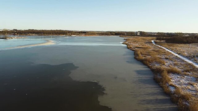 Frozen Ega Engso lake wetland bordered by snowy wetlands and reeds near Aarhus, Denmark, aerial establishing backdrop