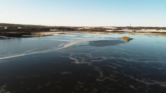 Frozen Ega Engso lake wetland with patterned ice and snowy shoreline near Aarhus, Denmark, aerial dolly over wispy frozen patterns