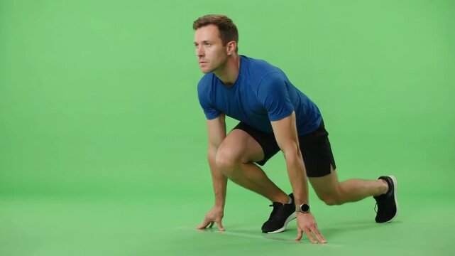 Athletic man in blue sportswear holding a low starting position against a bright green studio background