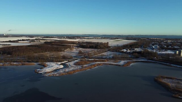 Frozen Ega Engso lake wetland and snow-covered countryside near Aarhus, Denmark in winter, aerial panoramic orbit overview