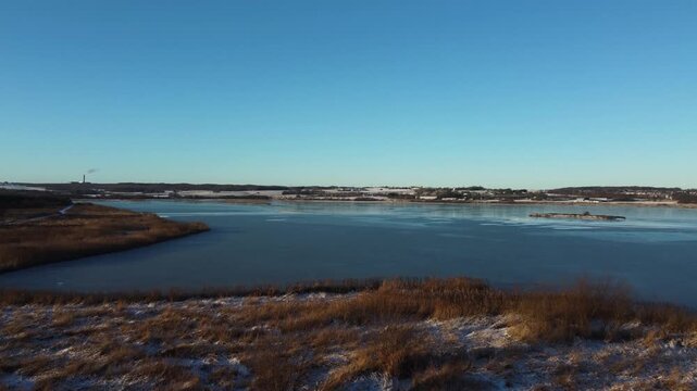 Winter wetland grasses overlook frozen Ega Engso lake wetland near Aarhus, Denmark under blue sky, aerial ascend reveal