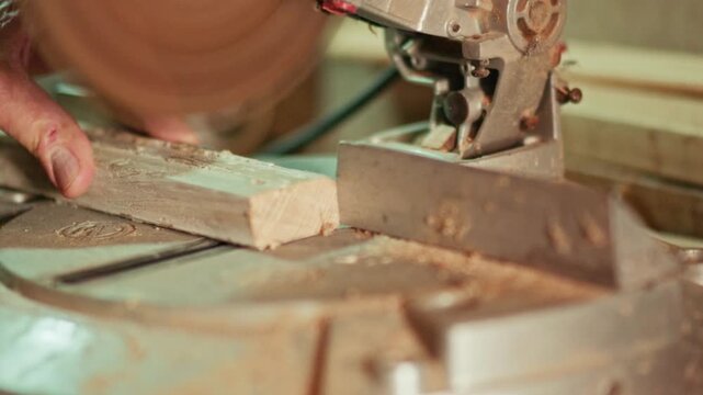 Slow motion close-up of a craftsman cutting a wooden strip with a miter saw in a workshop. Flying sawdust and precise blade action for carpentry, construction and maker projects