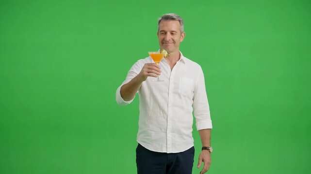 Smiling mature man in a white shirt holding an orange beverage with a straw against a bright green studio background