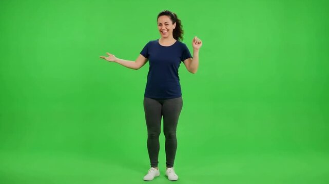 Smiling young woman dancing and gesturing energetically against a bright green studio background