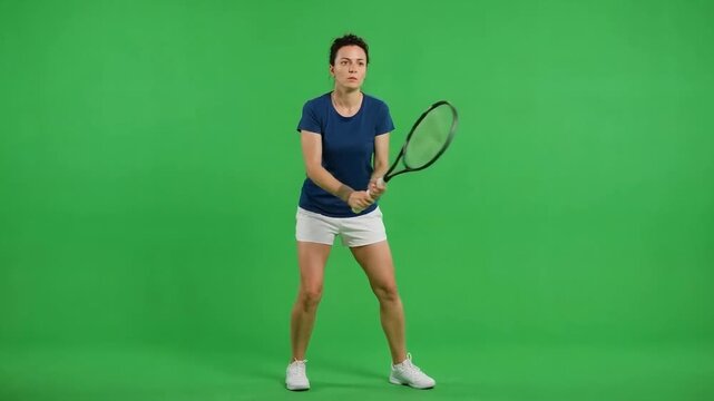 Young male tennis player standing alert with racket against a bright green studio background, ready for a forehand stroke
