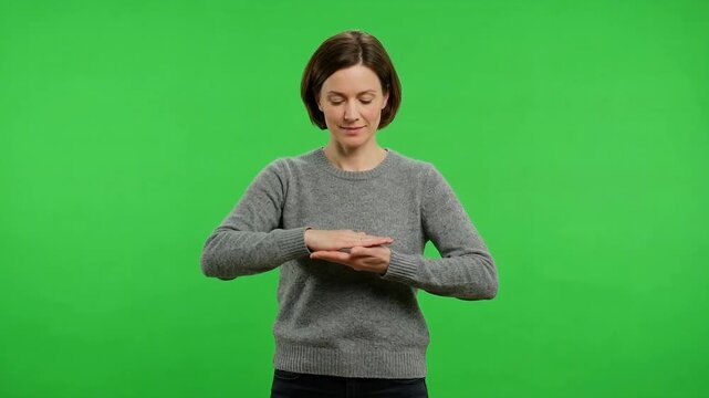Young woman in a gray sweater looking at her hands against a bright green chroma key background, isolated for compositing
