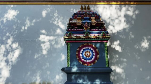 Moving shadows of leaves cast across a temple wall adorned with intricate traditional carvings