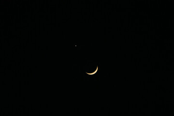Slender crescent moon appears alongside a bright celestial object, most likely the planet Venus. The night sky is dark, with no other visible objects or features. © Joshua Prasetyadi
