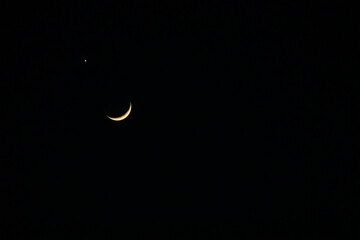 The crescent moon and the planet Venus shine in the dark night sky. Crescent moon and planet like Venus on dark night sky background. © Joshua Prasetyadi