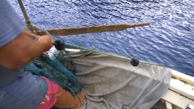 Fisherman hauls a fishing net by hand into a small boat on open water in natural habitat.