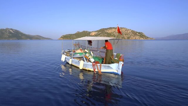 Turkish fisherman pulls a net by hand on an Aegean fishing boat with national flag visible.