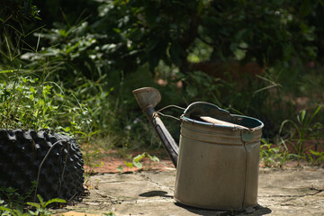 Vintage weathered metal watering can standing on concrete ground in rustic sunlit domestic garden © Nguyen Tuan