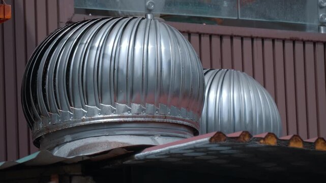 Shiny metallic wind turbine ventilators or wind exhaust fans, commonly referred to as whirlybirds are mounted on the roof to remove hot air and smoke from the home
