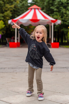 Excited little blonde girl fooling around and laughing at the striped canopy amusement park in an outdoor park