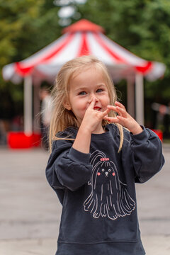 Excited little blonde girl fooling around and laughing at the striped canopy amusement park in an outdoor park
