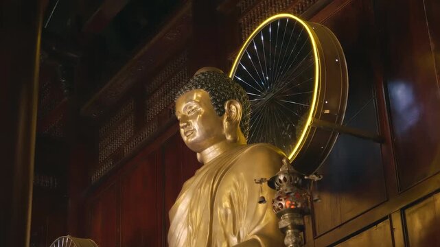 A golden statue of Buddha Shakyamuni with a cool cosmic LED halo with diverging and connecting beams of light behind the head stands on the altar in Chua Hai Duc Buddhist Temple in Nha Trang, Vietnam