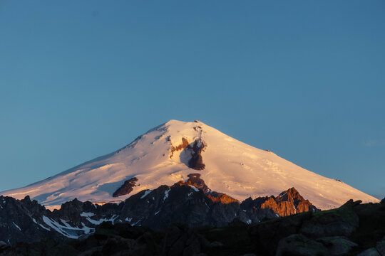 Broad snowy mountain summit glows in golden light above a dark jagged ridge in a clear sky landscape photograph for high altitude travel and dramatic wilderness backgrounds
