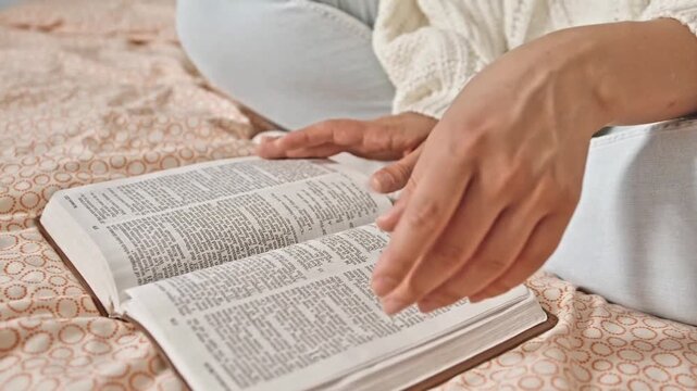 Close-up of Hands Turning the Pages of a Bible while Reading on a Bed at Home