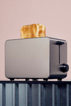 Toasted bread popping up in modern stainless steel toaster against pink background