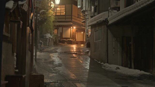 提灯の温かい明かりが灯る雪の温泉街の夜の石畳スローモーション